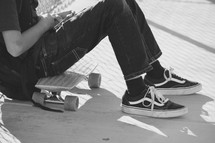a teen boy sitting next to his skateboard 