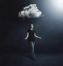 A woman under a rain cloud looking up to the bright light.