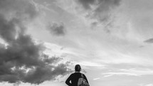 a woman with a backpack looking up at the sky 