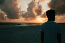 a silhouette of a young man standing on a beach at sunset 
