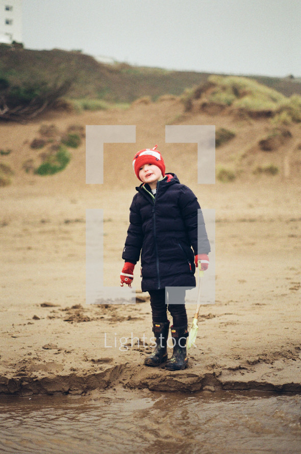a child in a beanie standing on a beach in winter 