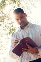 an African American man reading a Bible outdoors 