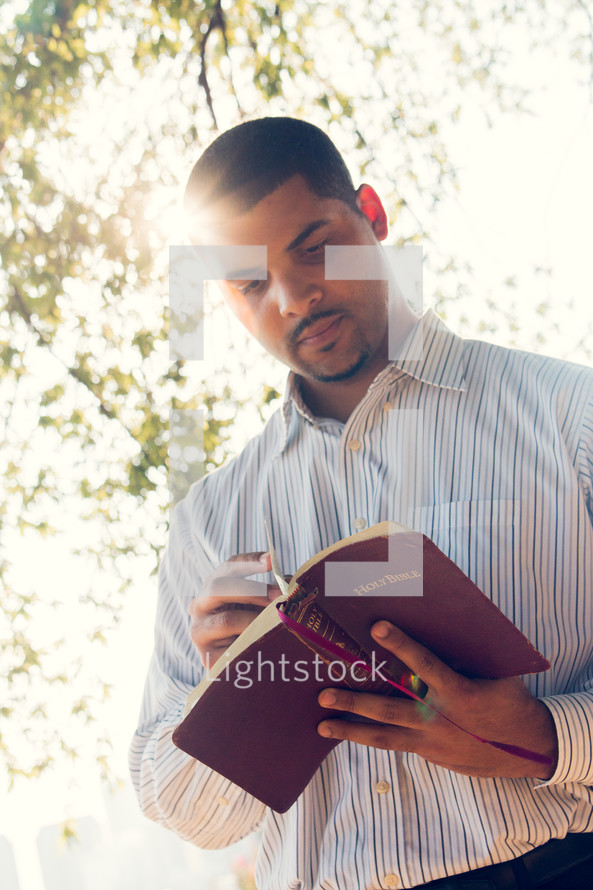 an African American man reading a Bible outdoors 