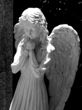 A statue of a female angel praying in black and white photography.