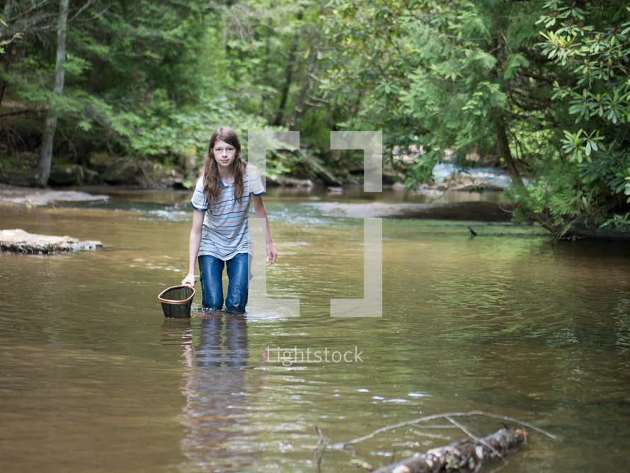 a teen girl with a net walking in a stream 