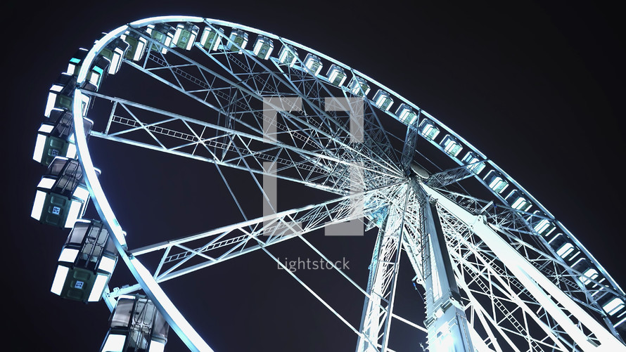 Brightly lit ferris wheel ride, which spinning at night or evening carnival. Low angle. Colored lights flashing. Concept of amusement park, fair, thrill. High quality photo