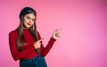 Happy smiling woman in red wear presenting and showing something isolated on pink background. Portrait of girl, she pointing with arms on her left with copy space