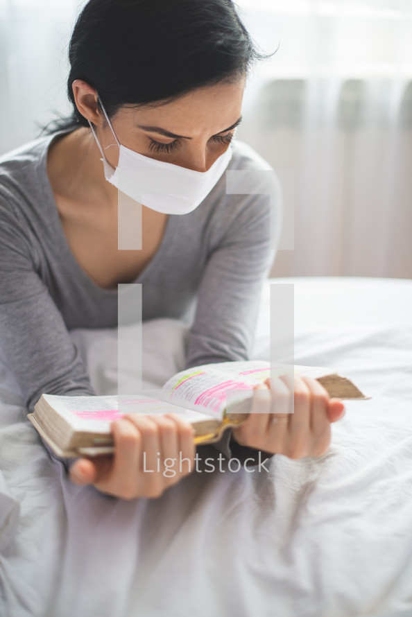 a woman wearing a mask reading a Bible 