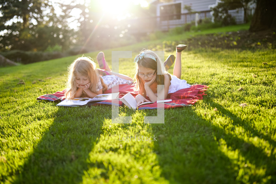 girls reading books on a blanket in grass 