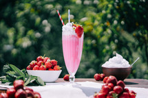 Still life - creamy strawberry milkshake cocktail or smoothie with straw on nature backdrop. Appetizing summer dessert. Healthy berry food. High quality 