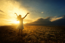 a woman with arms raised to God standing under the glow of sunlight 