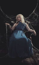 woman in a blue dress sitting in spider webs 