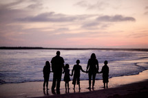 A family of six standing on a beach silhouetted against the sunset