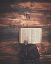 a boy reading a Bible on a wood floor 