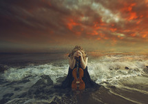 a woman with a viola kneeling in prayer in the ocean 