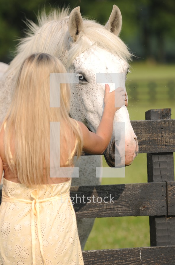 girl in a yellow sundress petting the head of a white horse