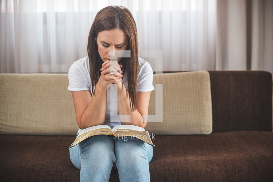 woman sitting on a couch praying with a Bible in her lap 