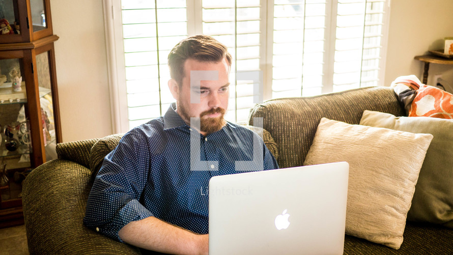 a man sitting on a couch typing on a laptop 