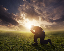 a man kneeling in prayer under the glow of the sun