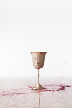 red wine spilling over a chalice onto a table 
