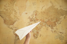 person flying a paper airplane in front of a world map.