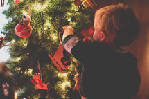 a toddler boy decorating a Christmas tree 