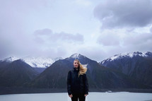 a woman standing in front of snow capped mountains with hair blowing in the wind 