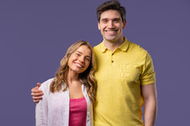 Pretty woman young adult man portrait on violet studio backdrop. Friendly couple smiling. Colorful vibrant outfit. High quality