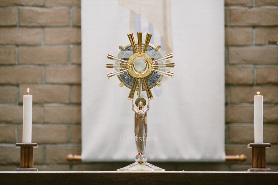 Table with a monstrance and candles in front o a brick wall.