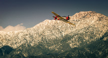 vintage single engine airplane flying over mountains 