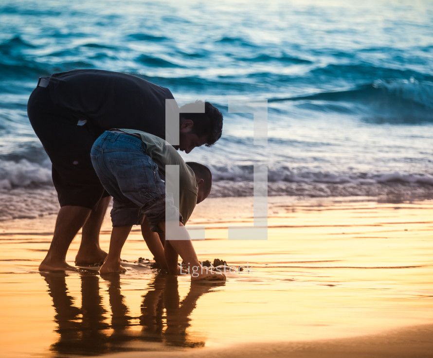 father and son digging in the sand on a beach 