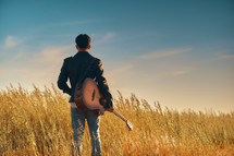 A young man standing in a field with a guitar