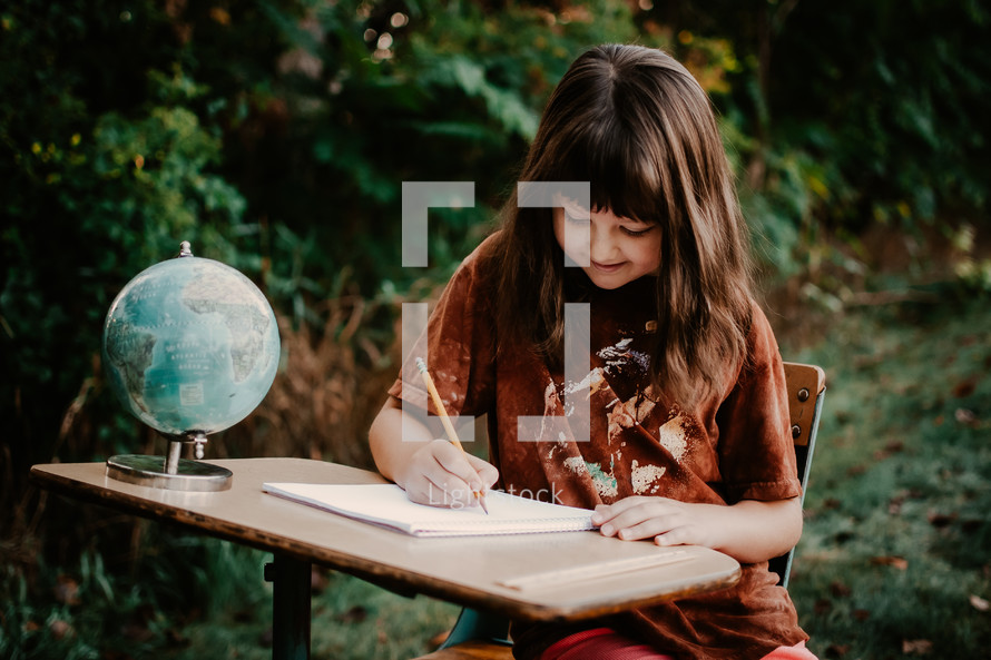 school girl writing at her desk with a globe