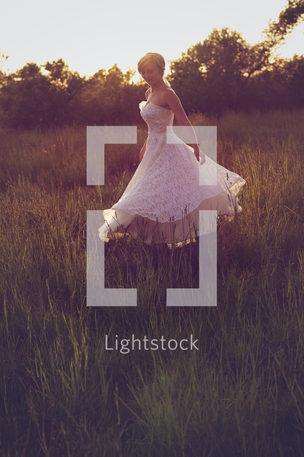 Woman in white dress twirling in a field of tall grass.