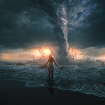 A woman bravely stands in front of a large tornado over the ocean.