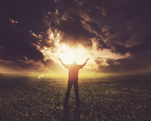 man standing with his arms raised in praise and worship to God under the glowing sun