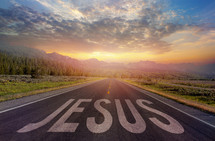 A road into a beautiful sunset with the word JESUS on the surface