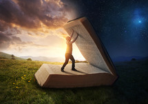 A man holding open a giant Bible between day and night.