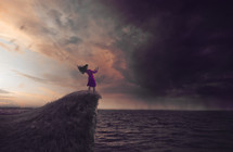 a woman standing at the edge of a cliff under a stormy sky reading a Bible 