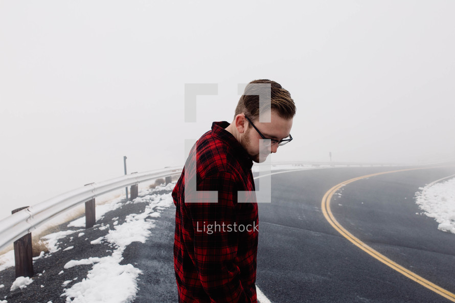 man in a plaid shirt looking down at a road 