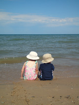 siblings sitting on a beach playing in the water 