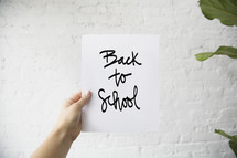 a man holding up a piece of white paper with the words back to school 