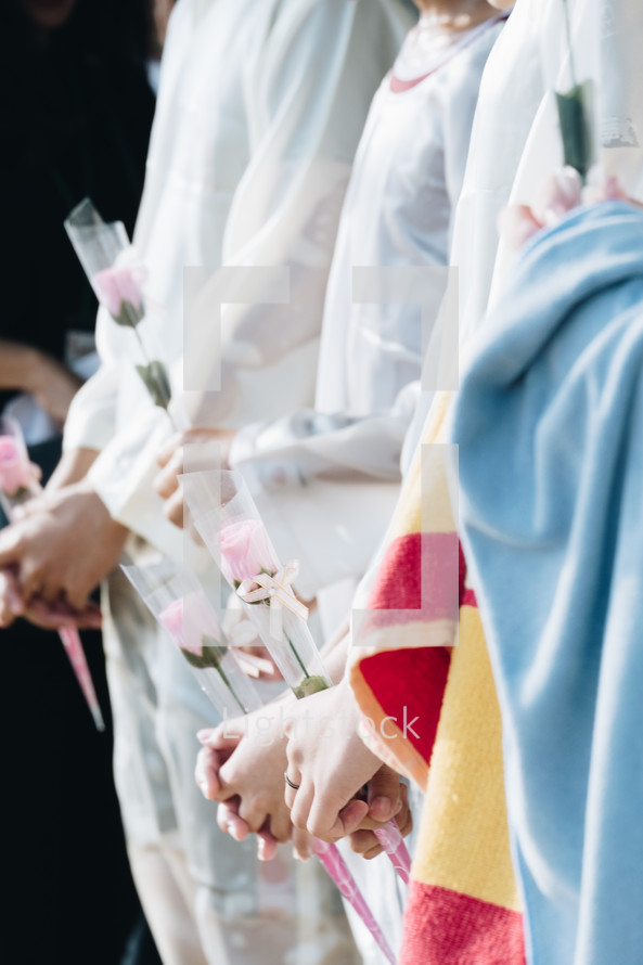 girls in white robes holding roses 