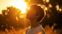 Portrait of a young boy meditating in the field at sunset.	