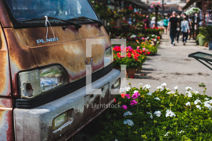 rusty van and flowers lining a city sidewalk 