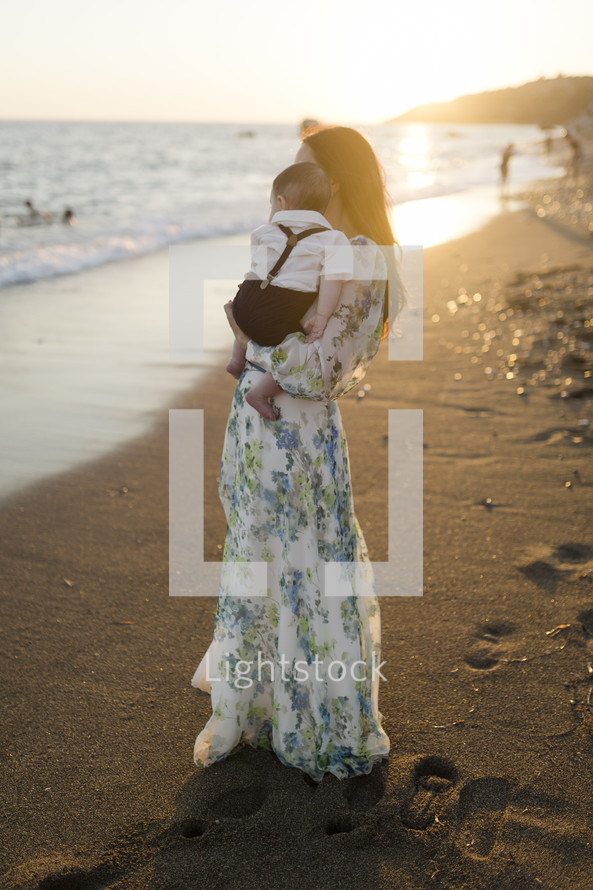Mother holding a baby on a beach at sunset.