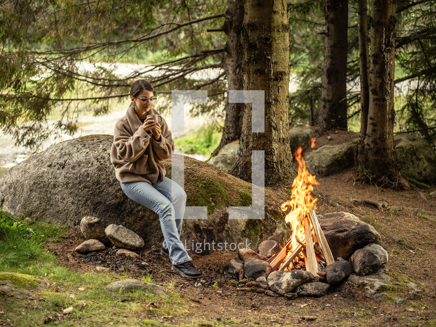 Woman sitting by campfire in a forest