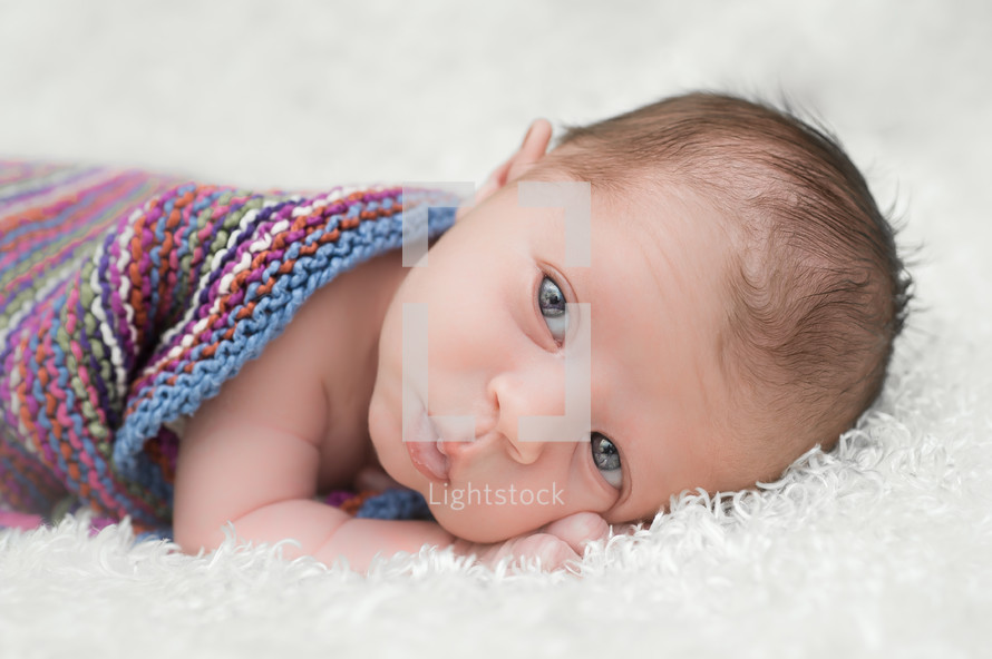 infant covered in a blanket lying on a white fuzzy rug