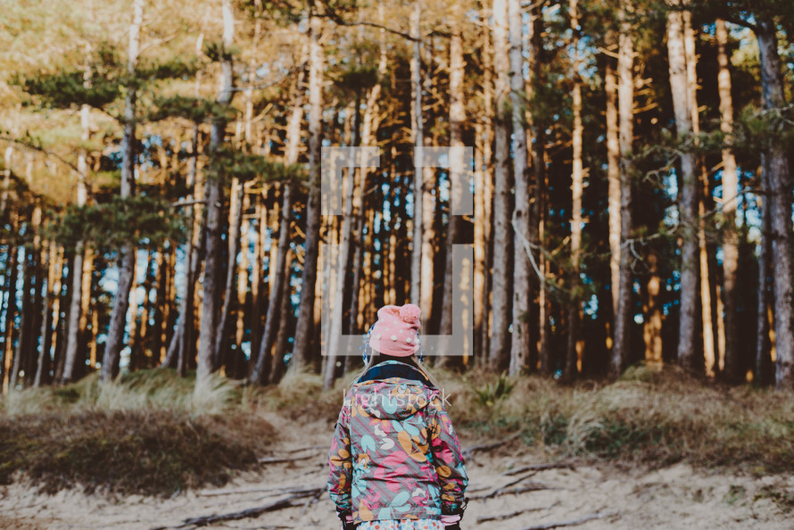 a girl in a coat walking into a forest