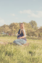 a pregnant mother sitting in the grass holding her belly 
